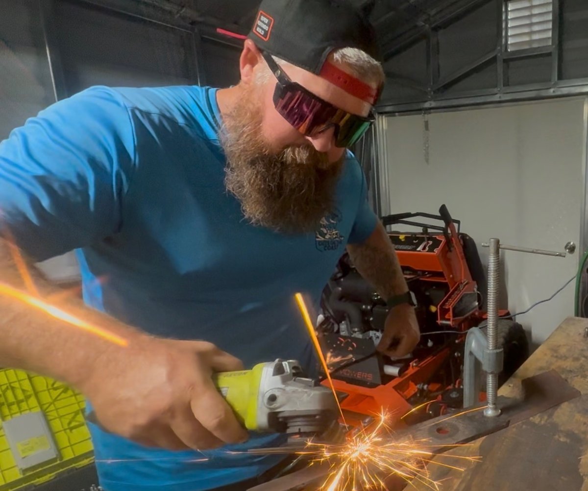 Sharpening a mower blade with an angle grinder, sparks flying, in the equipment trailer